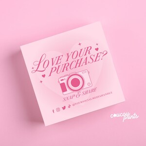May include: A square light pink card featuring a dark pink heart graphic, a camera icon, and the text LOVE YOUR PURCHASE? SNAP & SHARE. Below are social media icons and the placeholder text @YOURSOCIALMEDIAHANDLE, with coucou prints in the corner.
