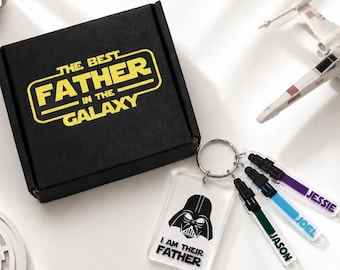 May include: A black gift box with the text "THE BEST FATHER IN THE GALAXY" in yellow. A keychain with a Darth Vader graphic and the text "I AM THEIR FATHER" is attached to three personalized keychains with names. A Star Wars themed gift.