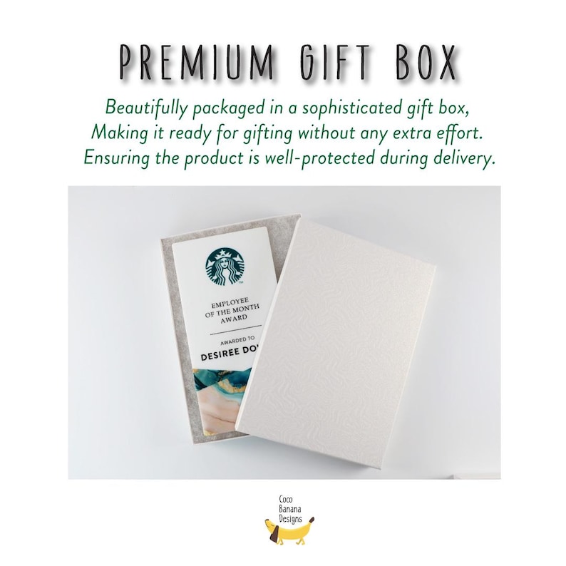 May include: White gift box with a textured lid, open to reveal a Starbucks Employee of the Month award. Text on the box reads "PREMIUM GIFT BOX". The award is in a gray felt holder. The Coco Banana Designs logo is in the bottom right.