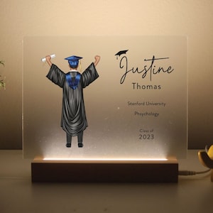 May include: A white acrylic light-up sign with a black silhouette of a graduate holding a diploma. The sign reads "Justine Thomas, Stanford University, Psychology, Class of 2023".