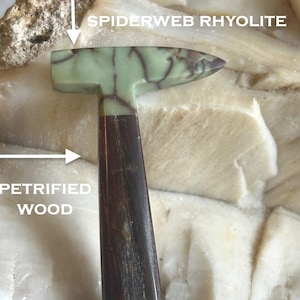 May include: A small hammer made of green and brown petrified wood. The hammer head is made of spiderweb rhyolite, a type of volcanic rock with a distinctive pattern. The handle is made of petrified wood, which has been preserved over time.