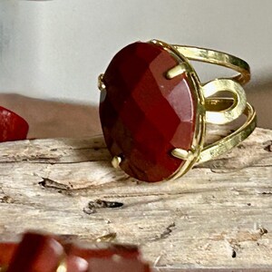 May include: A gold ring featuring a large, red, faceted gemstone. The ring has a simple, open band design.