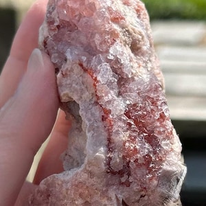 May include: A raw, natural crystal cluster with a mix of colors. The crystal features a base of light pink and white, with areas of deep red and clear crystal formations. The rough texture and unique color variations make it a striking specimen.
