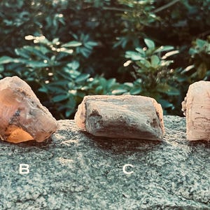 May include: Five different pink and white calcite crystals on a gray rock surface. The crystals are labeled A through E.