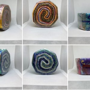 May include: Six fabric rolls, each with a different colorful pattern, are displayed on a white surface. The rolls are wrapped in plastic and have a hexagonal shape.