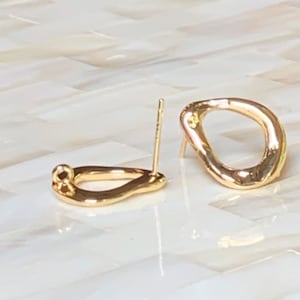 May include: A pair of gold-colored stud earrings. Each earring has an irregular, organic shape with a post for insertion. The earrings are displayed on a light-colored surface.
