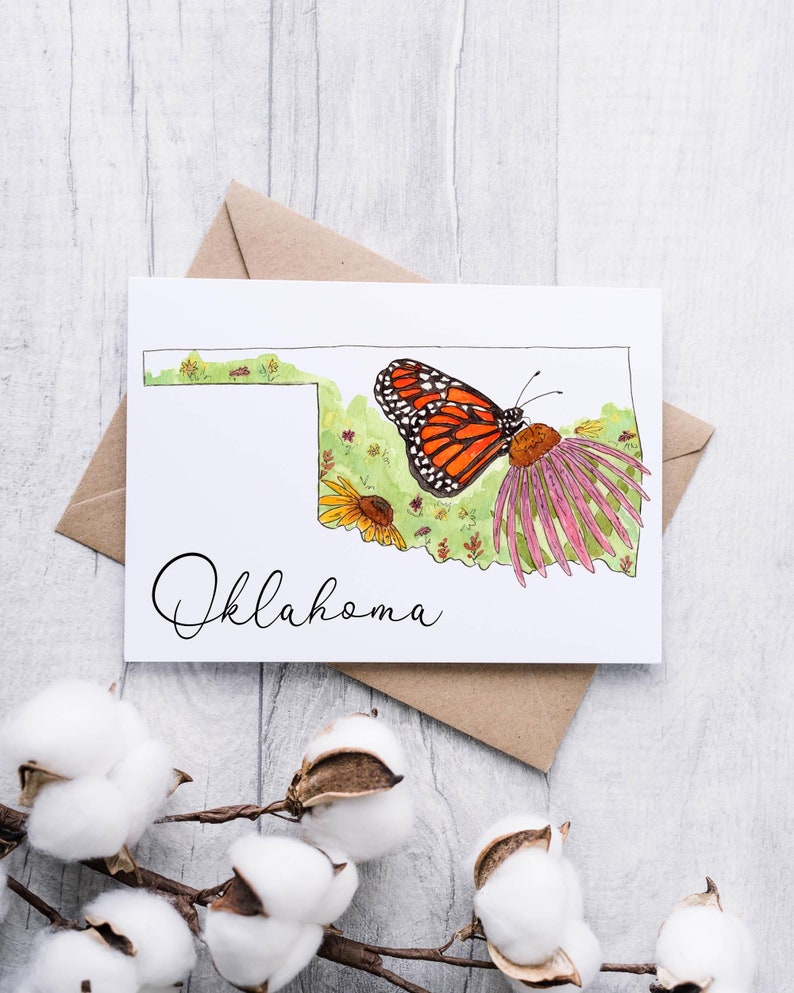 K&ouml;nnte beinhalten: Eine wei&szlig;e Karte mit einer Aquarell-Illustration des Bundesstaates Oklahoma. Die Illustration zeigt einen Monarchfalter, Wildblumen und das Wort "Oklahoma" in Kursivschrift.