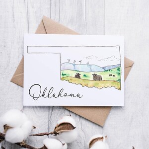 K&ouml;nnte beinhalten: Eine Aquarell-Illustration des Bundesstaates Oklahoma mit blauem Himmel, gr&uuml;nen H&uuml;geln, Windkraftanlagen und K&uuml;hen. Das Wort "Oklahoma" ist in Kursivschrift unterhalb der Staatsgrenze geschrieben.
