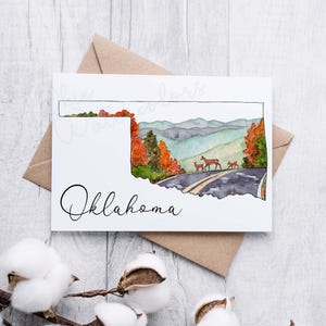 K&ouml;nnte beinhalten: Ein Aquarellbild des Bundesstaates Oklahoma mit einer Stra&szlig;e und Hirschen im Hintergrund. Der Text "Oklahoma" steht unterhalb der Staatsgrenze.