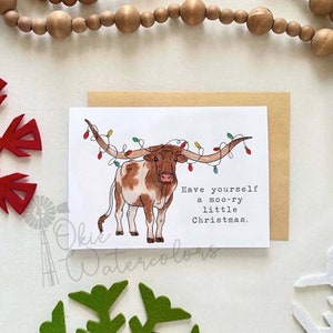 May include: A Christmas card featuring a cartoon illustration of a brown and white Texas Longhorn steer with a string of colorful Christmas lights wrapped around its horns. The text on the card reads "Have yourself a moo-ry little Christmas."