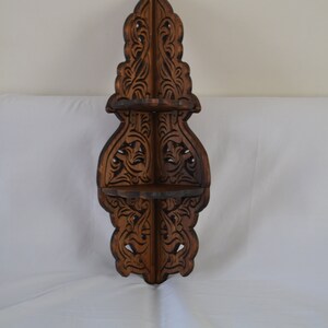 May include: A dark brown wooden corner shelf with intricate carvings. The shelf has three tiers and is designed to fit in a corner.