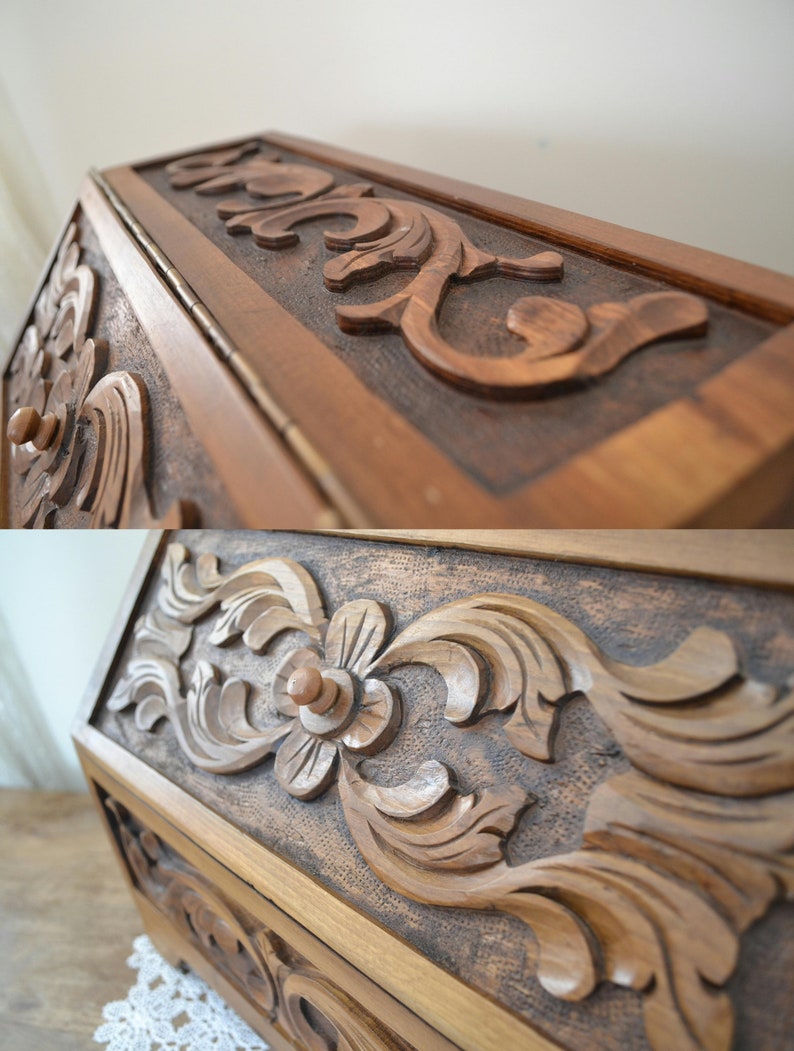 May include: A wooden box featuring intricate hand-carved floral and scrolling leaf patterns on its exterior panels. The wood has a medium brown finish with a textured, darkened background behind the raised, smooth-carved decorative elements.