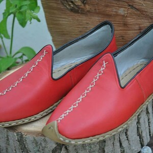 Puede incluir: Un par de zapatos rojos de cuero sin cordones con costuras blancas y suela marr&oacute;n.