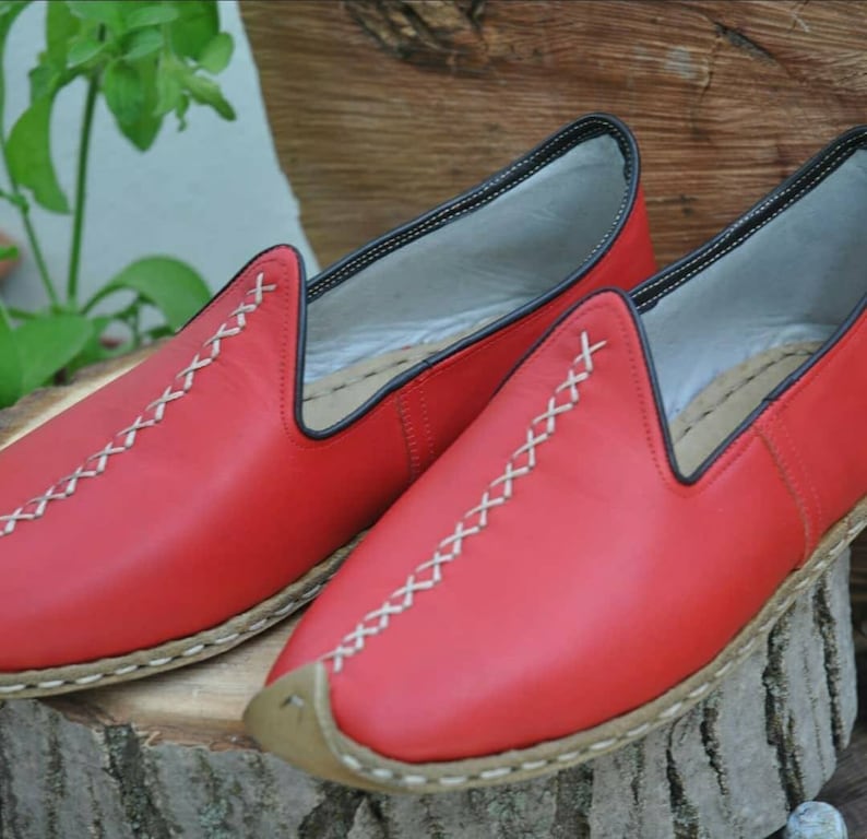 Puede incluir: Un par de zapatos rojos de cuero sin cordones con costuras blancas y suela marr&oacute;n.