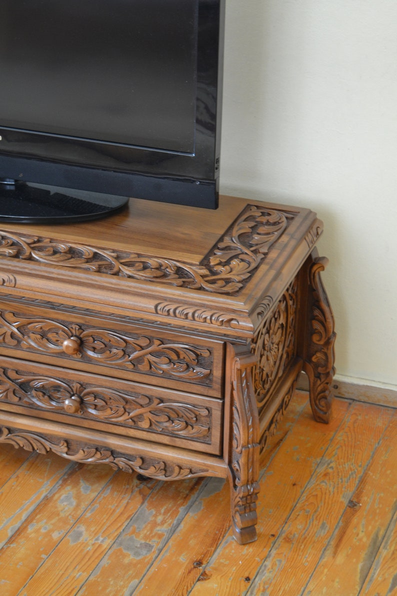 Puede incluir: Un mueble de TV de madera oscura con intrincados tallados. El mueble tiene tres cajones y se apoya en cuatro patas. El mueble est&aacute; hecho de madera maciza y tiene un acabado rico y oscuro.