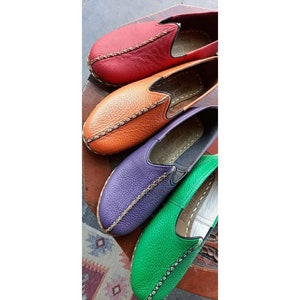 Puede incluir: Cuatro pares de zapatos de cuero sin cordones en diferentes colores: rojo, naranja, morado y verde. Cada zapato tiene un detalle de puntada decorativa y las palabras "Hecho a mano en Turqu&iacute;a" en la plantilla.