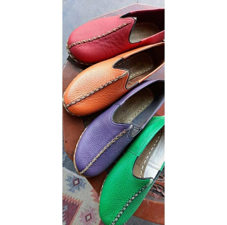 Puede incluir: Cuatro pares de zapatos de cuero sin cordones en diferentes colores: rojo, naranja, morado y verde. Cada zapato tiene un detalle de puntada decorativa y las palabras "Hecho a mano en Turqu&iacute;a" en la plantilla.