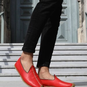 Puede incluir: Zapatos rojos de cuero con cordones blancos y suela marr&oacute;n. Los zapatos son usados por una persona con pantalones negros.