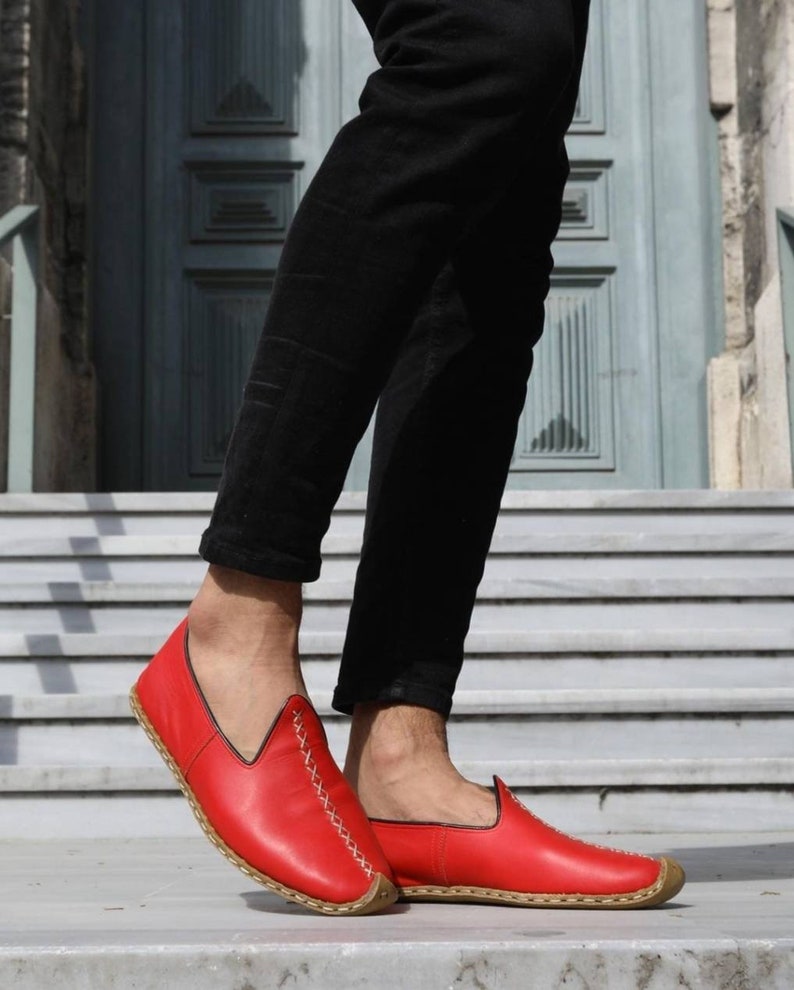 Puede incluir: Zapatos rojos de cuero con cordones blancos y suela marr&oacute;n. Los zapatos son usados por una persona con pantalones negros.