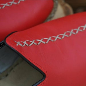 Puede incluir: Primer plano de un par de zapatos de cuero rojo con un detalle de costura blanca. Los zapatos tienen un ribete negro alrededor de la abertura.