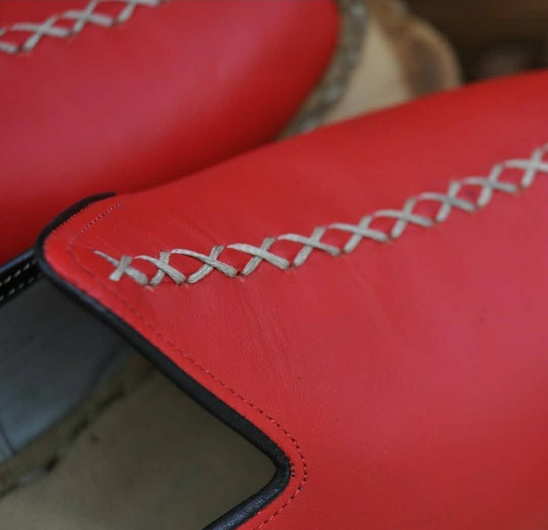 Puede incluir: Primer plano de un par de zapatos de cuero rojo con un detalle de costura blanca. Los zapatos tienen un ribete negro alrededor de la abertura.