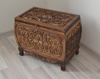May include: A wooden chest with intricate carvings of floral patterns. The chest has a dark brown finish and is decorated with a border of small metal studs.
