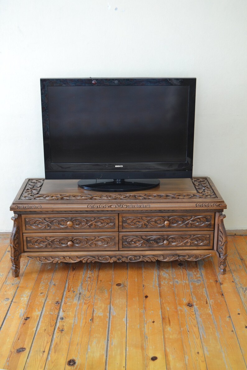 Puede incluir: Un mueble de TV de madera oscura con tallas intrincadas y tres cajones. El mueble est&aacute; sobre un suelo de madera.