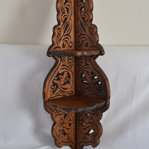 May include: A dark brown wooden corner shelf with intricate carved details. The shelf has three tiers and is designed to fit in a corner.