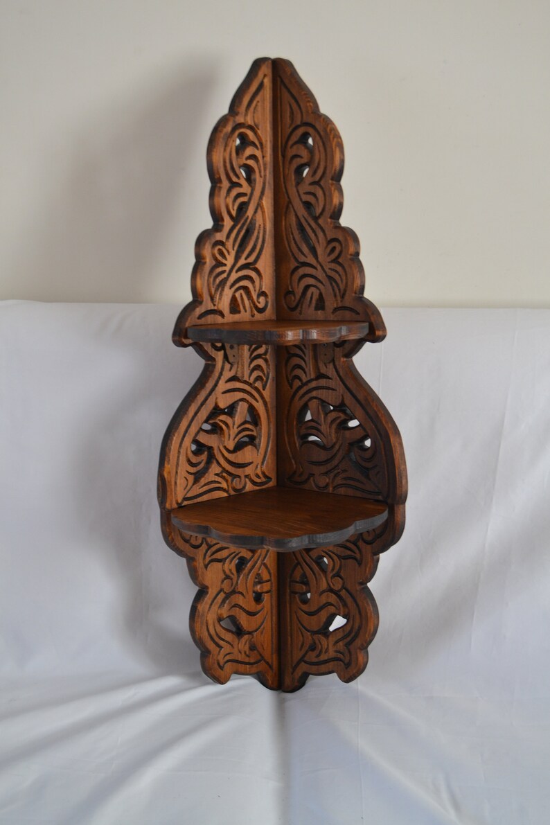 May include: A dark brown wooden corner shelf with intricate carved details. The shelf has three tiers and is designed to fit in a corner.