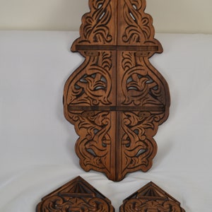 May include: A set of three intricately carved wooden wall decor pieces. The main piece is a tall, vertical design with a brown stain. Two smaller pieces are shaped like a diamond and have a similar design.