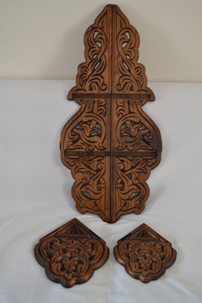 May include: A set of three intricately carved wooden wall decor pieces. The main piece is a tall, vertical design with a brown stain. Two smaller pieces are shaped like a diamond and have a similar design.