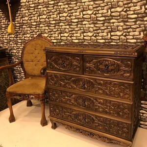 Puede incluir: Una c&oacute;moda de madera marr&oacute;n oscuro con cinco cajones, cada uno tallado intrincadamente con dise&ntilde;os florales. La c&oacute;moda tiene patas ornamentadas y una parte superior ligeramente curvada.