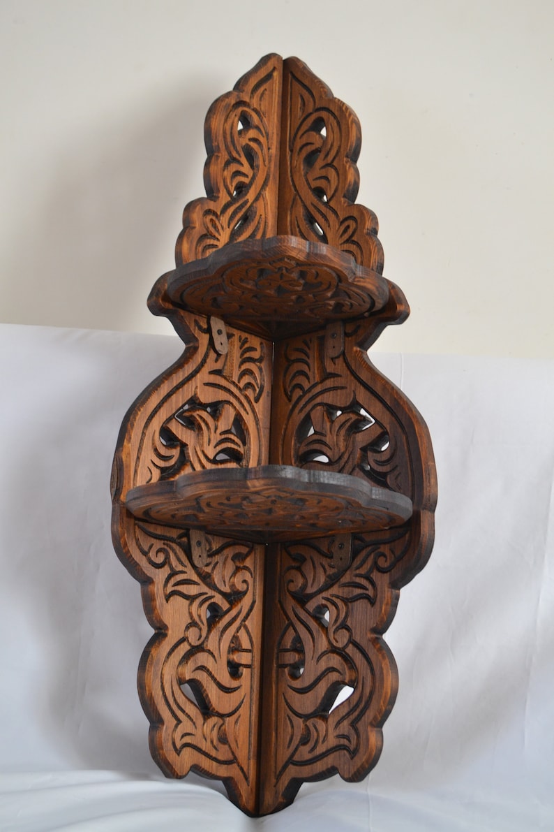 May include: A dark brown wooden corner shelf with intricate carvings. The shelf has three tiers and is designed to fit in a corner.