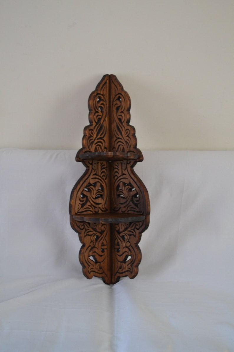 May include: A dark brown wooden corner shelf with intricate carvings. The shelf has three tiers and is designed to fit in a corner.