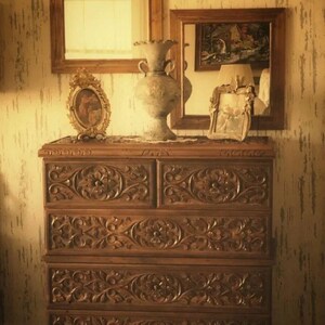 Puede incluir: Una c&oacute;moda de madera con cinco cajones, cada uno tallado intrincadamente con motivos florales. La c&oacute;moda est&aacute; decorada con un jarr&oacute;n, una imagen enmarcada y dos espejos.