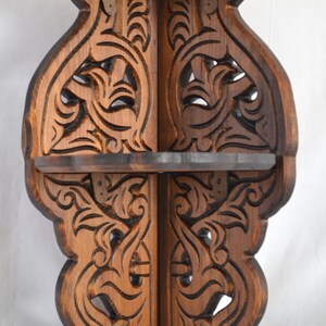May include: A wooden corner shelf with intricate carvings in a dark brown finish. The shelf has three tiers and is designed to fit in a corner.