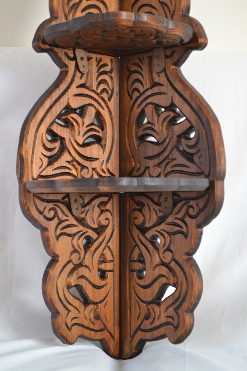 May include: A wooden corner shelf with intricate carvings in a dark brown finish. The shelf has three tiers and is designed to fit in a corner.