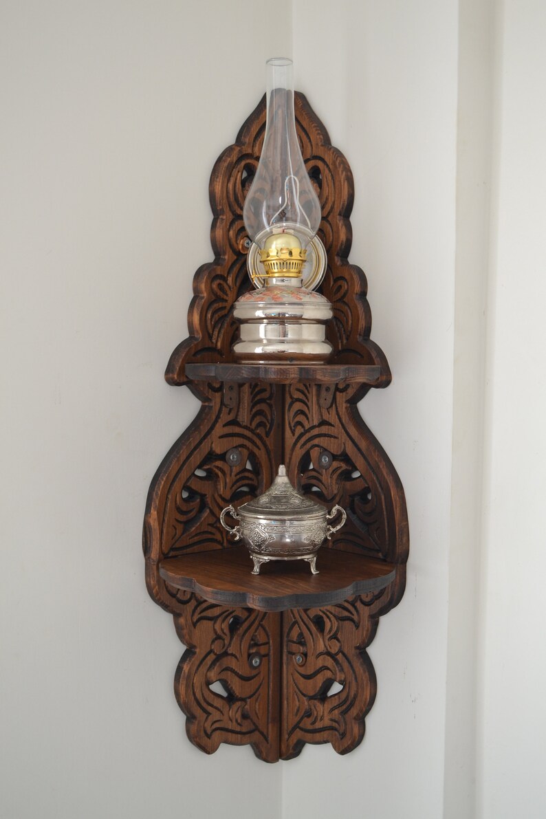May include: A dark brown wooden corner shelf with intricate carvings. The shelf has two tiers and features a silver oil lamp with a glass chimney and a silver sugar bowl.
