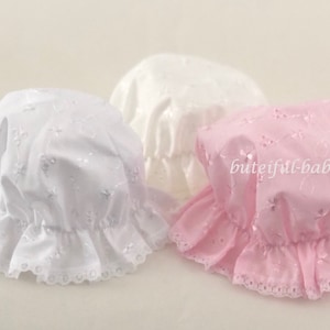 May include: Three baby bonnets, one white and two pink, with delicate lace trim and embroidered floral designs.