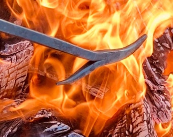 May include: A close-up of a metal fireplace poker in a roaring fire. The flames are orange and yellow, and the poker is partially submerged in the burning wood.