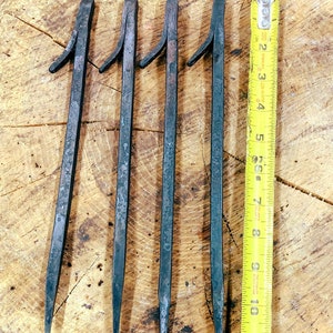 May include: Four metal rods with a pointed tip and a curved handle. The rods are approximately 11 inches long and are arranged in a row on a wooden surface. A yellow measuring tape is placed next to the rods.