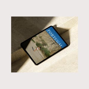 May include: A magazine cover with the word "PORTUGAL" in large blue letters on a blue background. The cover features a photo of a person in a white swimsuit standing in a desert landscape.