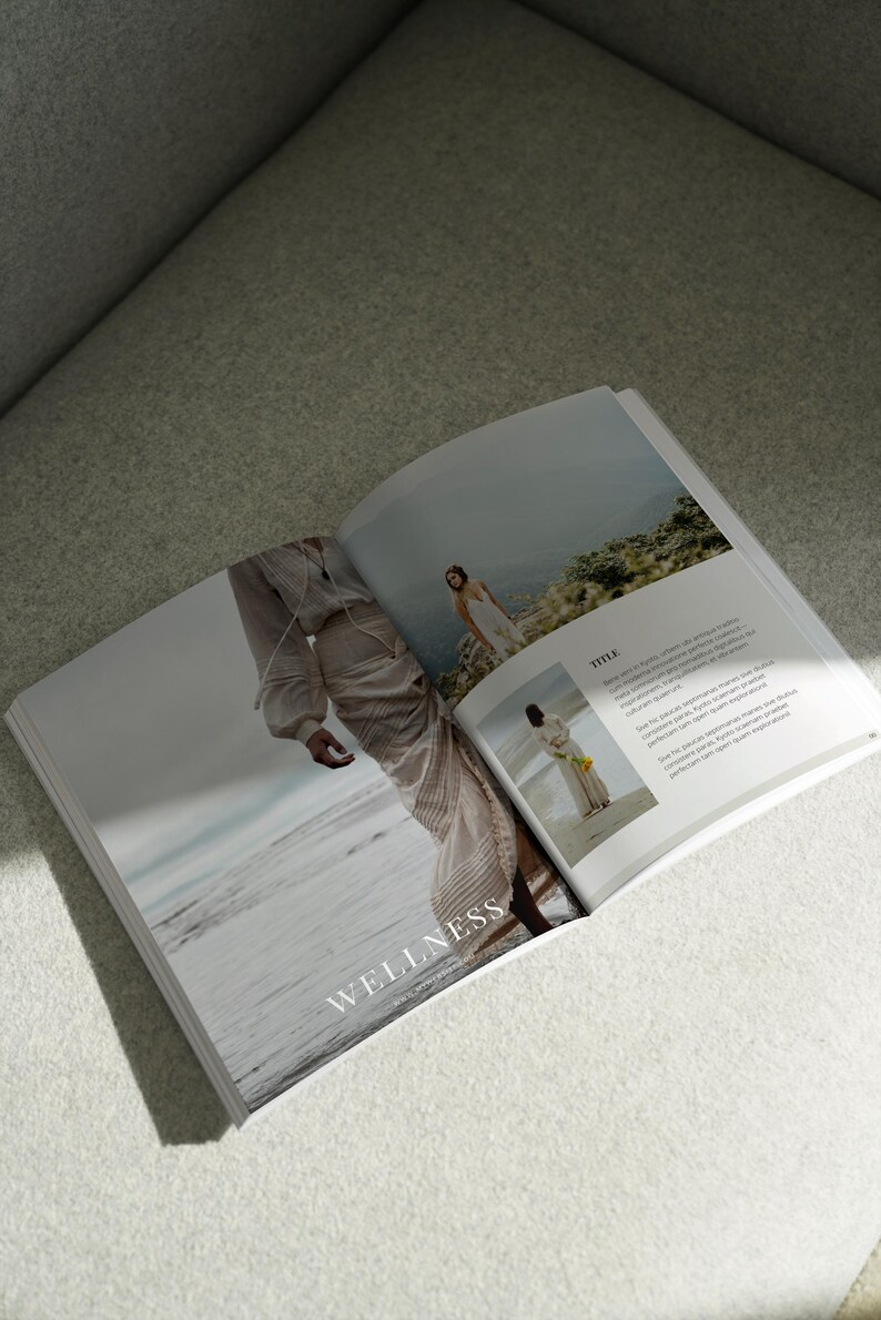 May include: Open magazine with the word "WELLNESS" on the cover. The magazine features a woman in a flowing white dress walking on a beach and another woman in a white dress standing on a cliff.