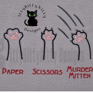 May include: A gray fabric design featuring a black cat logo with green eyes and the text "MyBittyKitty Designs". Below the logo are embroidered cat paws representing "Rock", "Paper", "Scissors", and "Murder Mitten" in red text.