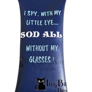 Puede incluir: Un estuche para gafas de piel sintética azul con un gato negro y el texto "I SPY, WITH MY LITTLE EYE..... SOD ALL WITHOUT MY GLASSES!" y "Itty Bit Des" en bordado blanco.