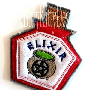 May include: A red and white felt patch with a cauldron and the word "ELIXIR" embroidered on it.