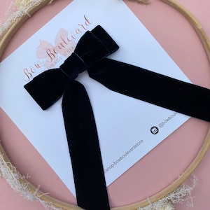 Puede incluir: Un lazo para el pelo de terciopelo azul marino con una cola larga. El lazo está atado en un nudo clásico y se muestra sobre un fondo blanco con el texto "Bow Boulevard Handmade Hair Bows" y el nombre de usuario de las redes sociales "@bowboulevardstore".