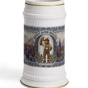 May include: A white ceramic beer stein with gold trim and a textured beaded rim. The center features a graphic of a Bigfoot character in traditional alpine clothing holding a beer mug, with the text "BIGFOOT ALPINE BEER HALL" and "PROST FROM THE PINES".