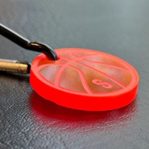 May include: A bright red keychain featuring a basketball design. The basketball has a white outline and the number 8 inside.