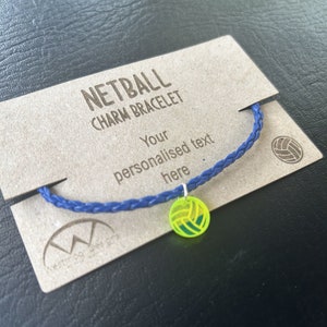 May include: A blue braided bracelet with a yellow and green netball charm. The bracelet is displayed on a brown card with the text "Netball Charm Bracelet" and "Your personalised text here".